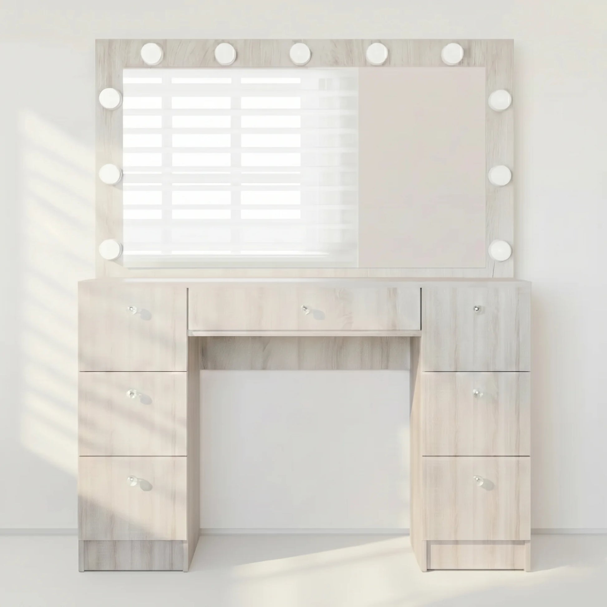 A light wood vanity table with a large rectangular mirror framed by round light bulbs, shown in a bright, minimalist room setting.